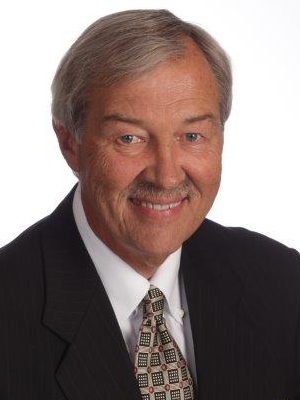 Donald Tuttle older man with grey hair wearing a black suit white shirt and brown pattern tie