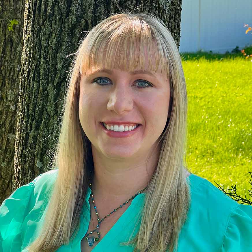 Blonde woman blues eyes wearing a teal shirt and necklace