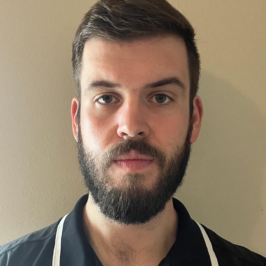 Man dark hair and beard wearing a navy collard shirt