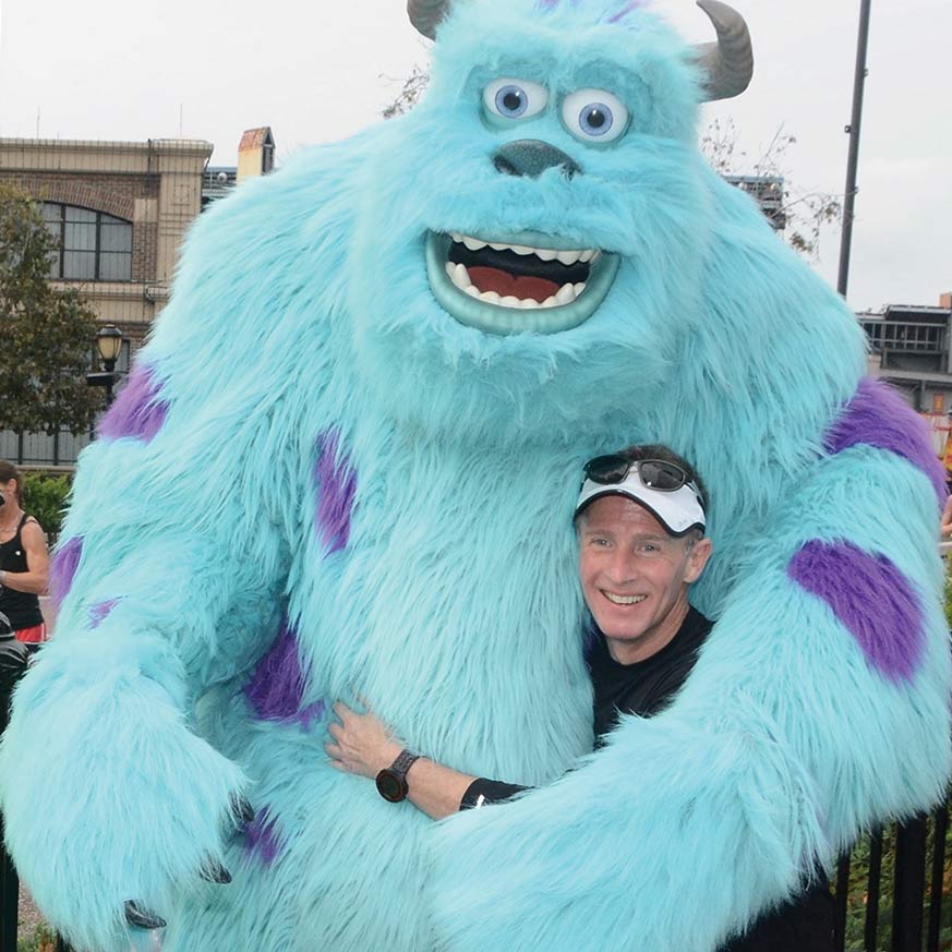 white man in athletic wear at Disney hugging Sullyfrom monsters inc