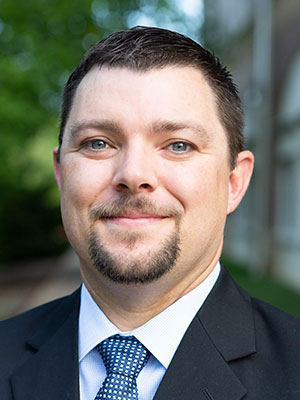 Man wearing a suit with dark brown hair and beard