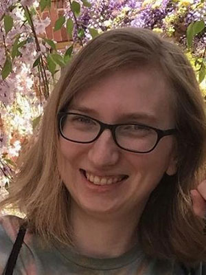 Blonde woman standing in front of pink flowers wearing black glasses