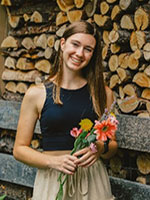 Girl with brown hair holding flowers standing in front of stacked wood