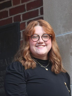 white woman with red hair wearing glasses a black shirt with gold necklaces