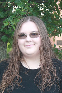 woman with light brown long wavy hair wearing a balck shirt and dark glasses