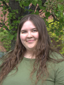 woman with light brown long wavy hair wearing a balck shirt and dark glasses