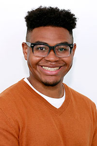Man with brown skin wearing black glasses and orange sweater