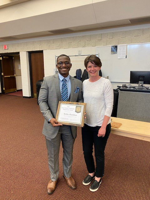Black man in grey suit holding award standing next to white woman short brown hair