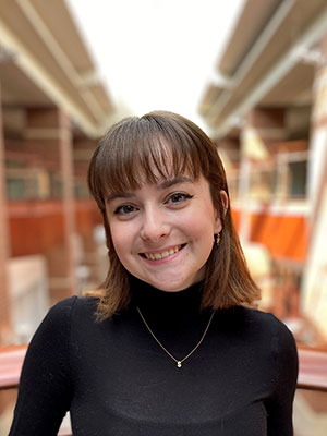 Smiling young lady wearing a black long sleeve shirt. She has short brown hair and bangs.