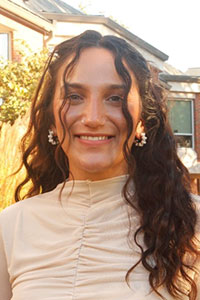 woman with dark brown wavy hair wearing a cream color shirt