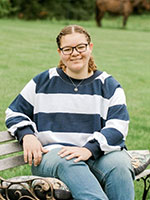 Girl wearing glases  and a stripped blue and white shirt with curly light brown hair.