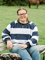 Girl wearing glasses  and a striped blue and white shirt with curly light brown hair.