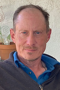 Man with brown hair and blue eyes wearing a blue shirt and brown pullover half zip sweater