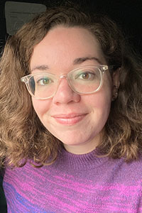 woman with light brown hair wearing glasses and a pink sweater