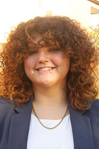 woman with curly red hair and lip piercing wearing a dark grey suit jacket