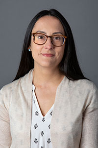 woman with glasses and long dark hair wearing a white blouse and cream sweater