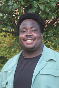 man with brown skin black hair wearing a black shirt and mint jacket