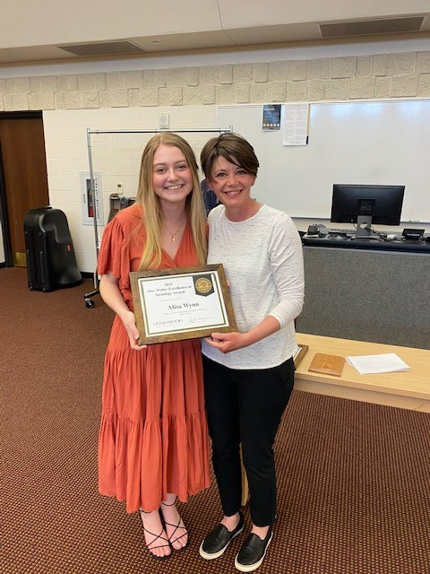 White woman wearing a coral dress holding award standing next to a white woman with short brown hair