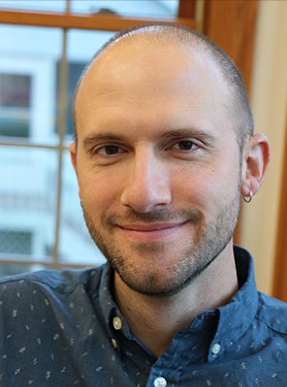Bald white man with dark beard and earring wearing a blue button up shirt