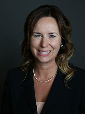 Jo Anna Pollock woman with brown hair and blue eyes wearing a black suit and pearl necklance