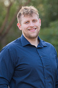 White man with light brown hair wearing a dark blue button up shirt