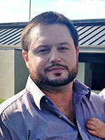 Man with dark hear and beard standing outside wearing a dress shirt