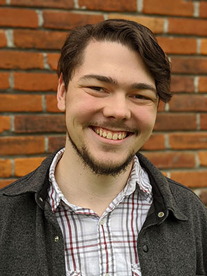 Man with brown hair in a button up shirt with jacket.