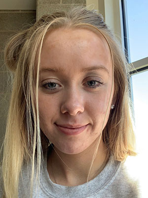 white woman blonde hair blue eyes smiling at camera in front of window