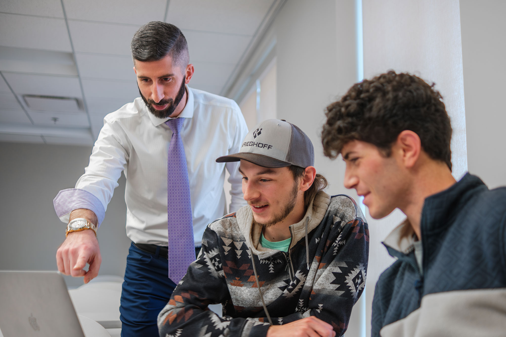 Students working on laptop assisted by professor