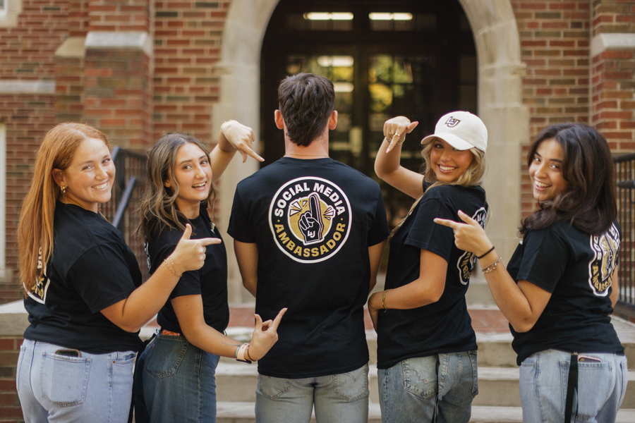 social media ambassador students pointing at the back of an ambassador shirt with logo