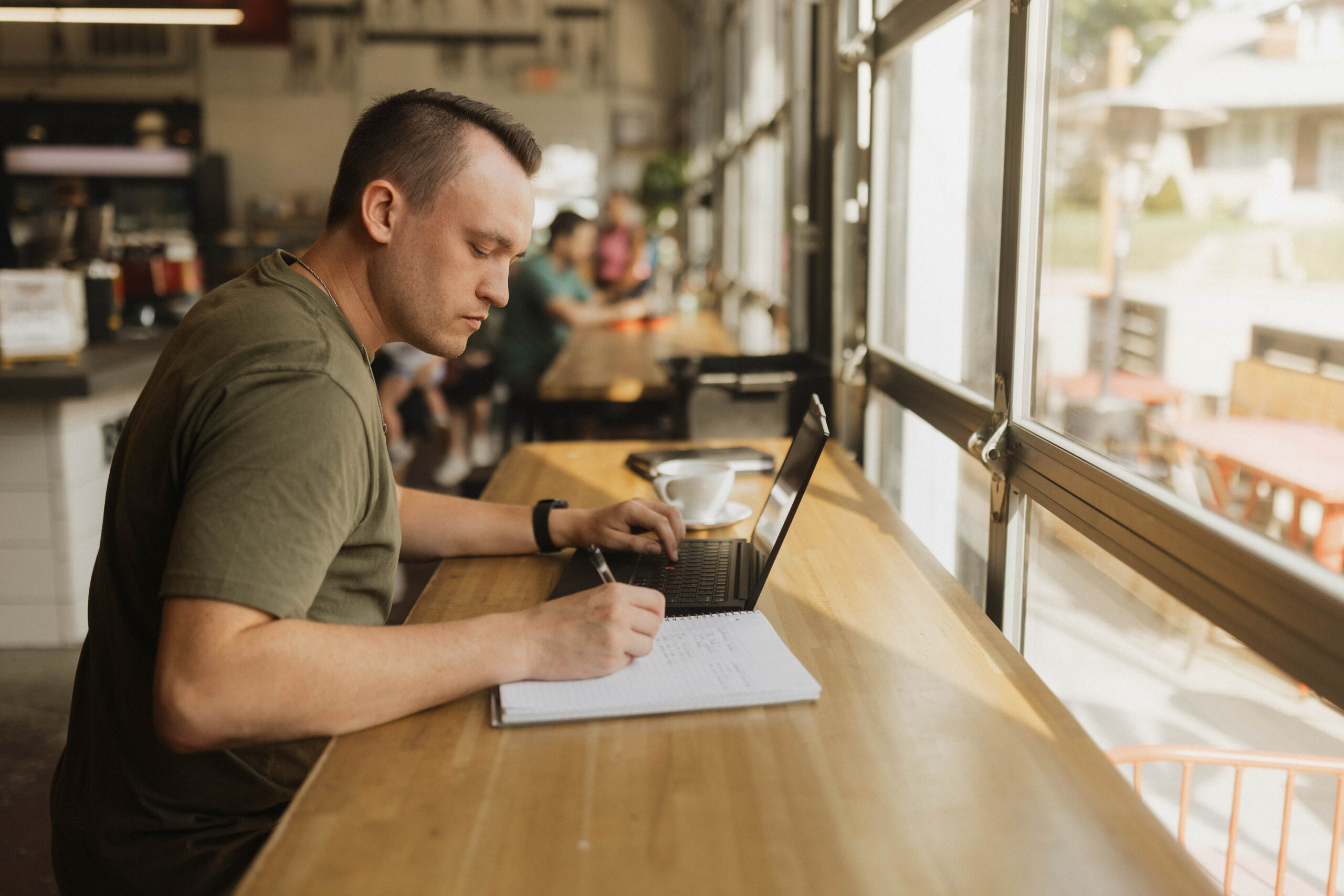 male adult learner taking notes in a notebook while watching a lecture on a laptop